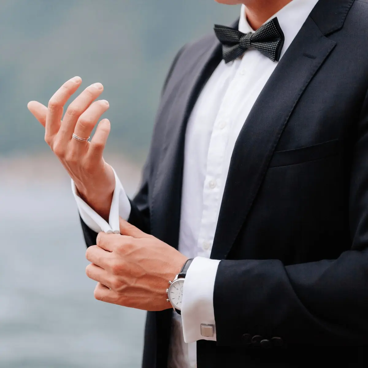A man in a black tuxedo adjusting his cufflink, custom tailored by The Suit Doctor